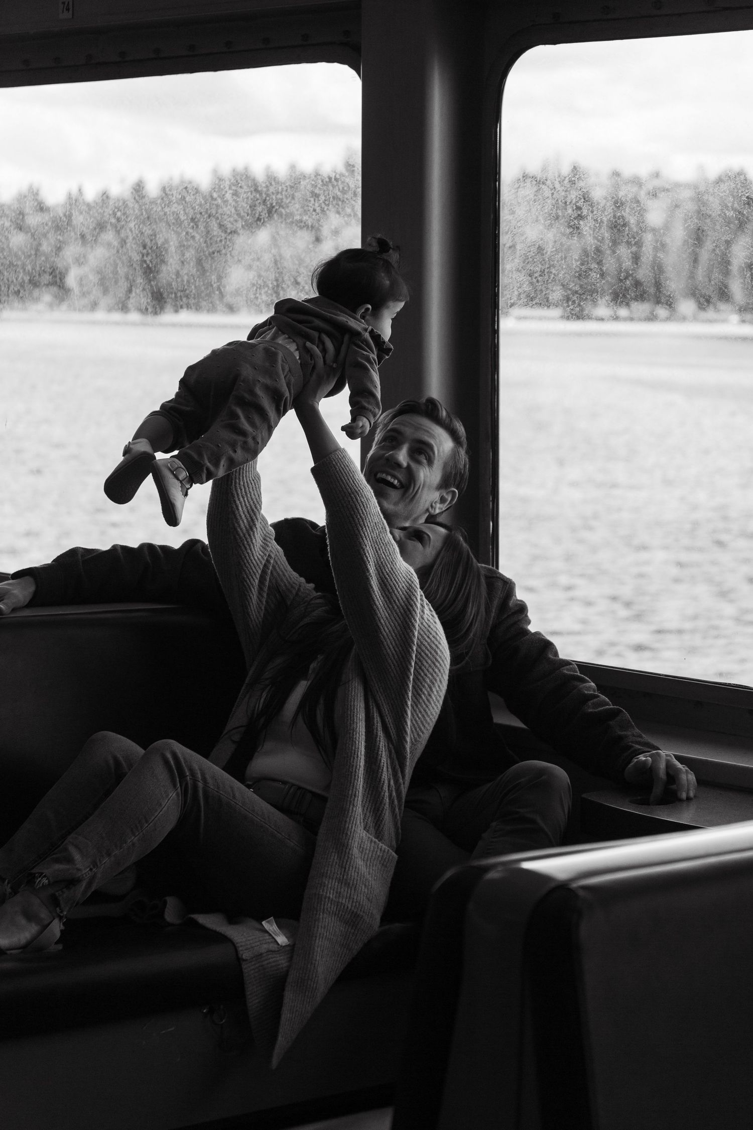 Playful moment captured on ferry boat with water and trees visible through window.