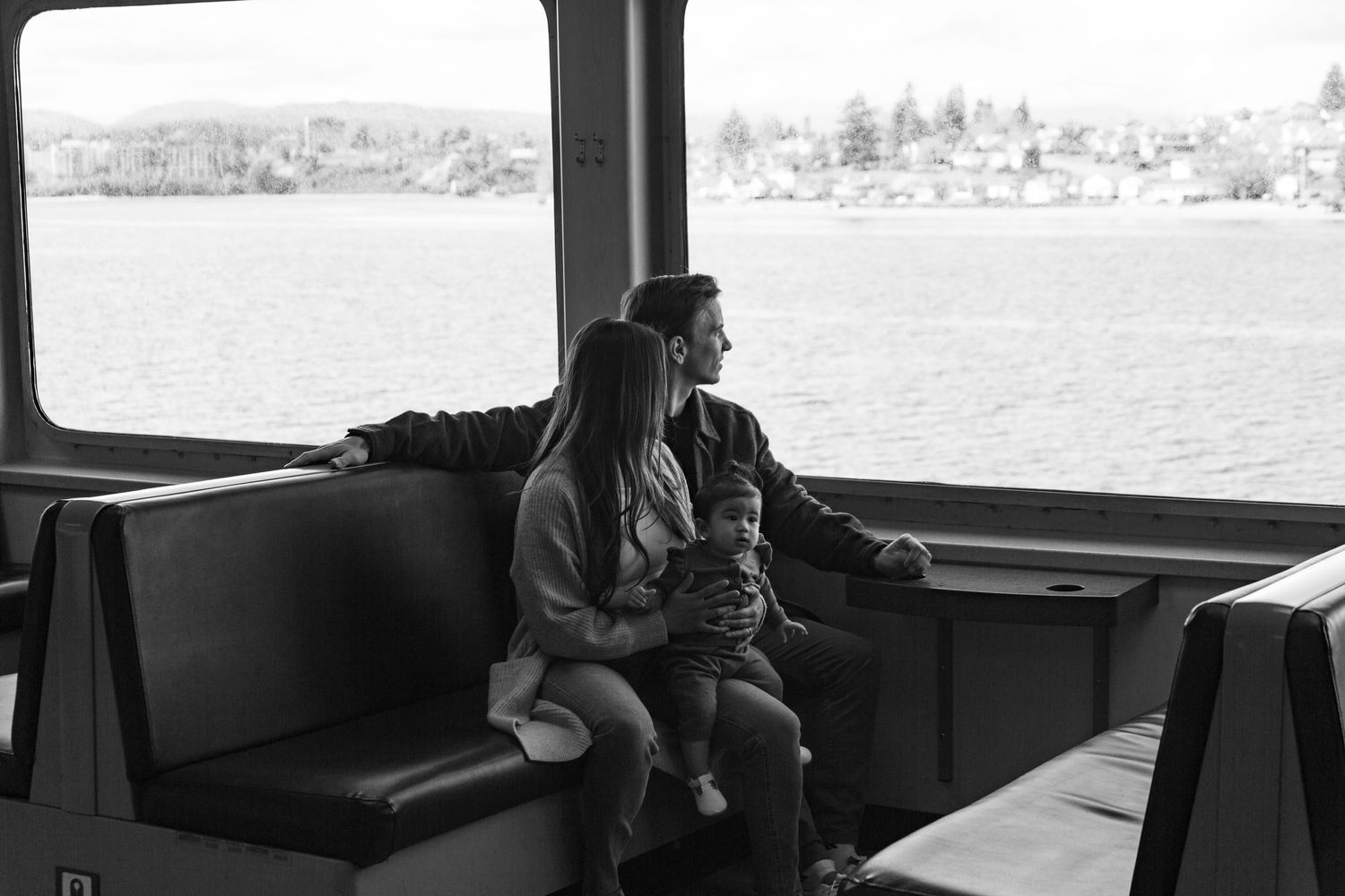A couple sits together on a ferry bench looking out at the waterfront view.