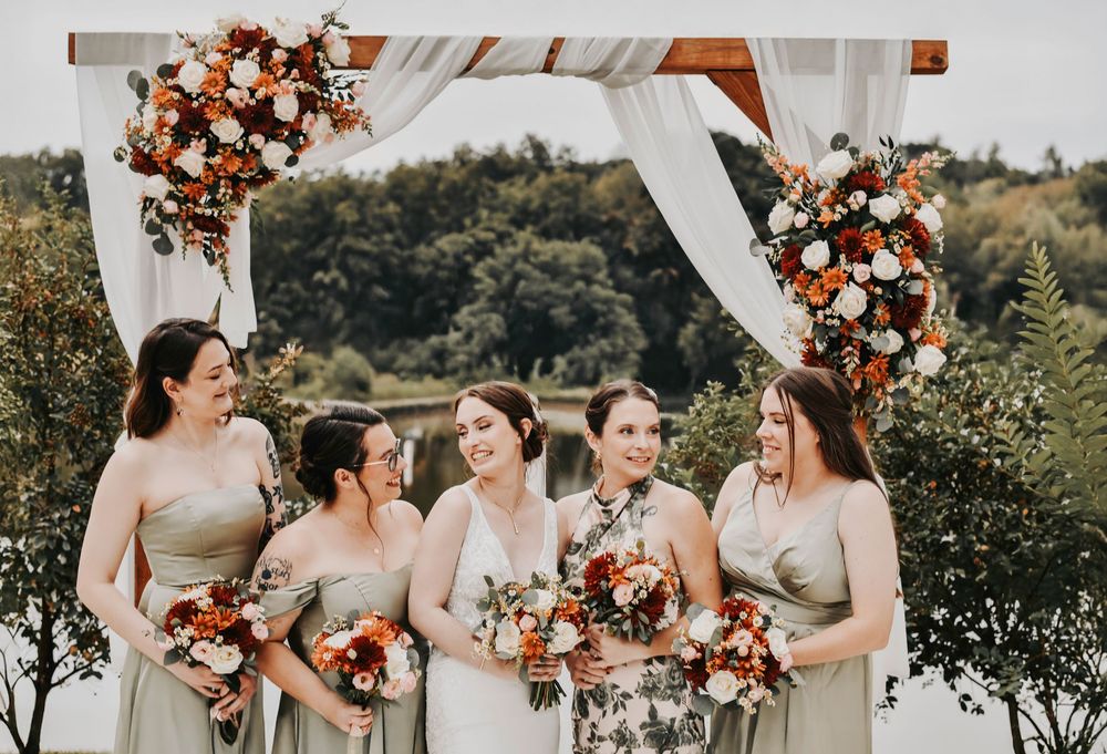a happy photo of a bridal party in green and botanical florals holding fall florals and wild flowers