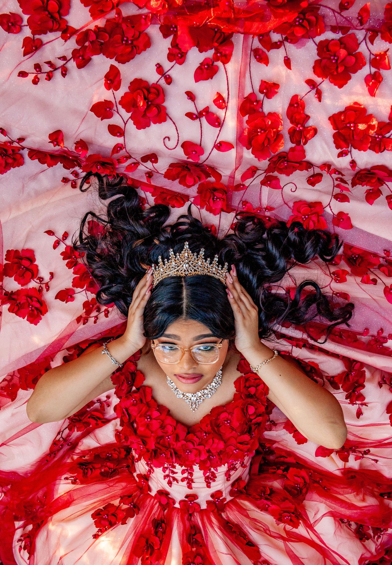 Overhead shot of quinceañera dress with red floral details and crystal crown.