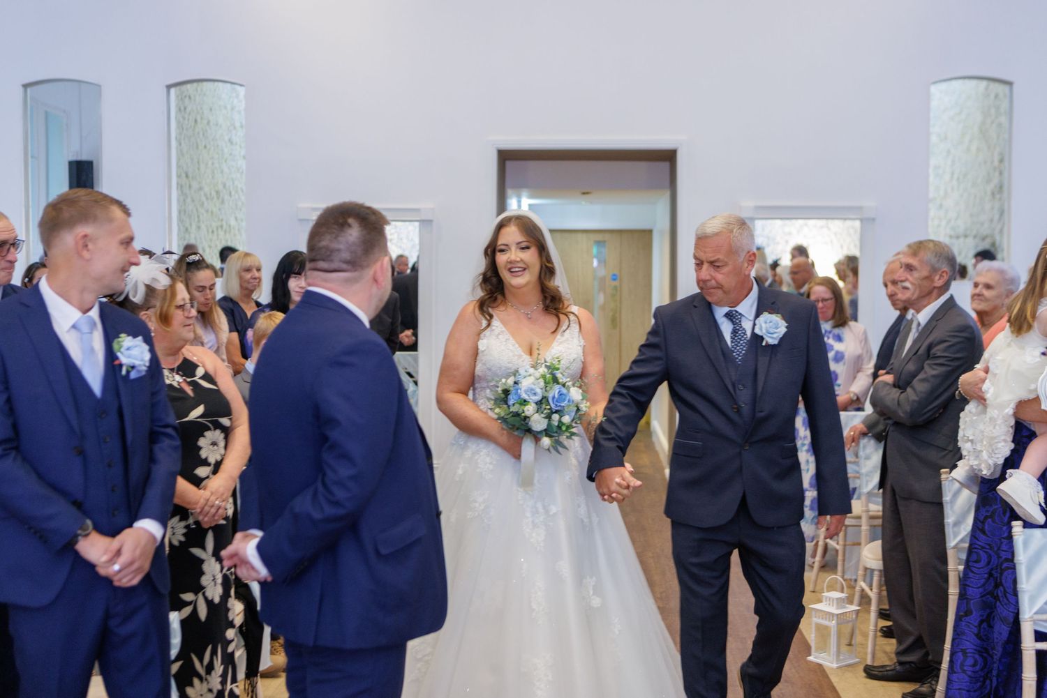 Wedding guests applaud during a celebration in a bright indoor venue with white decor.