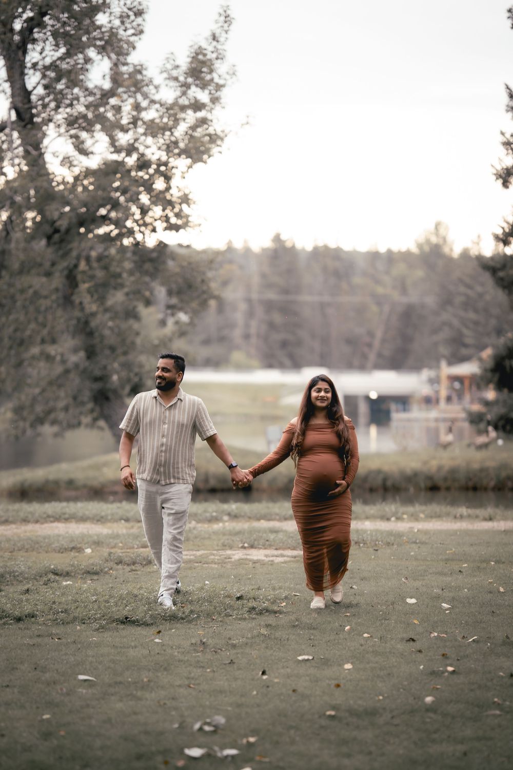 A couple holds hands while walking through a serene park setting during golden hour.