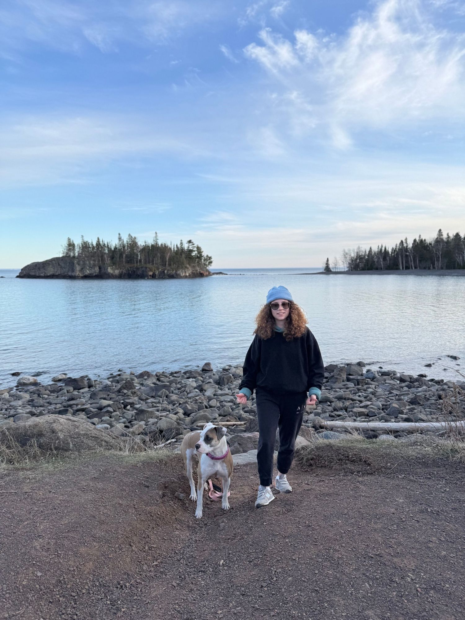 A scenic view of rocky shoreline with small islands on Lake Superior, featuring someone walking their dog on a clear day.