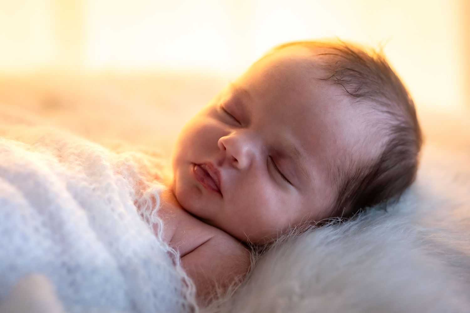 Peaceful newborn baby sleeping wrapped in white lace, bathed in warm golden light.