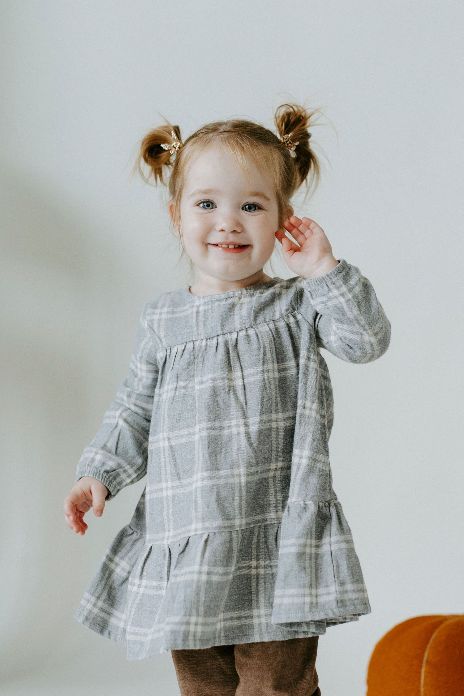A child in a gray plaid dress poses with an orange pumpkin against a white background.