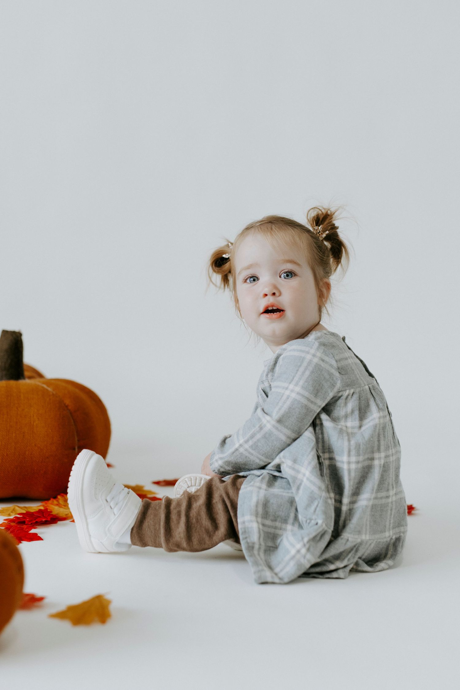 A series of photos showing a small child in a plaid shirt sitting and playing near autumn pumpkins against a white backdrop.