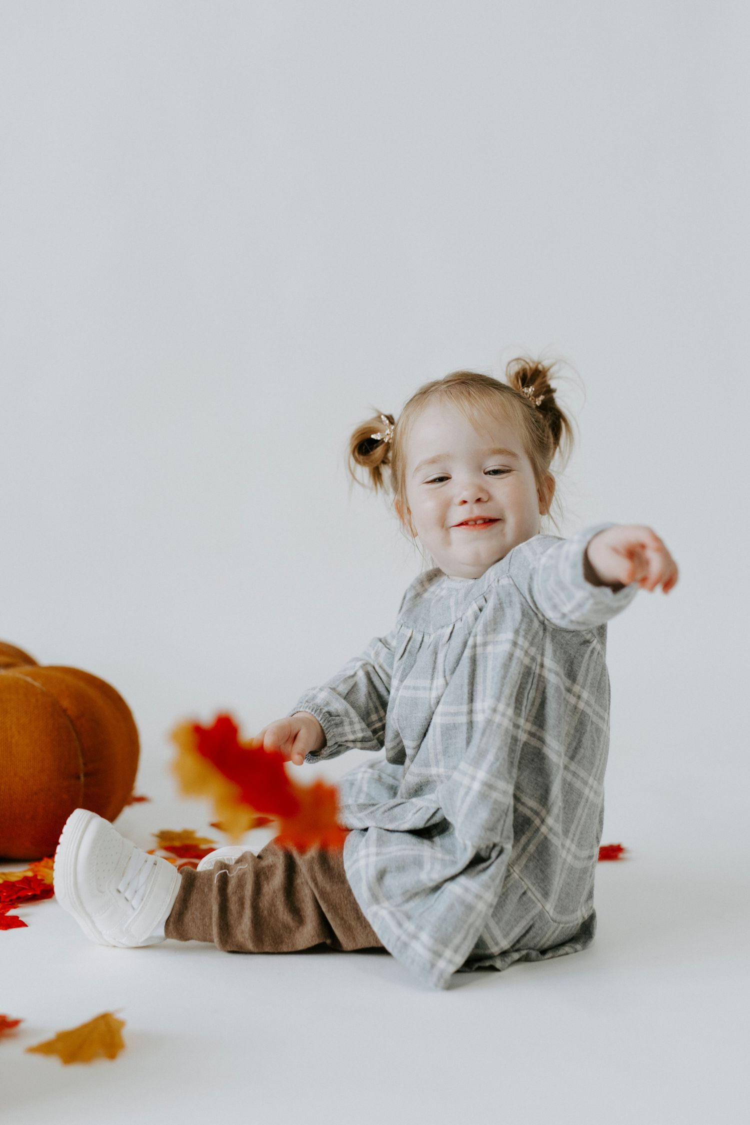 A small child in a gray outfit playing on a white studio floor with autumn decorations.