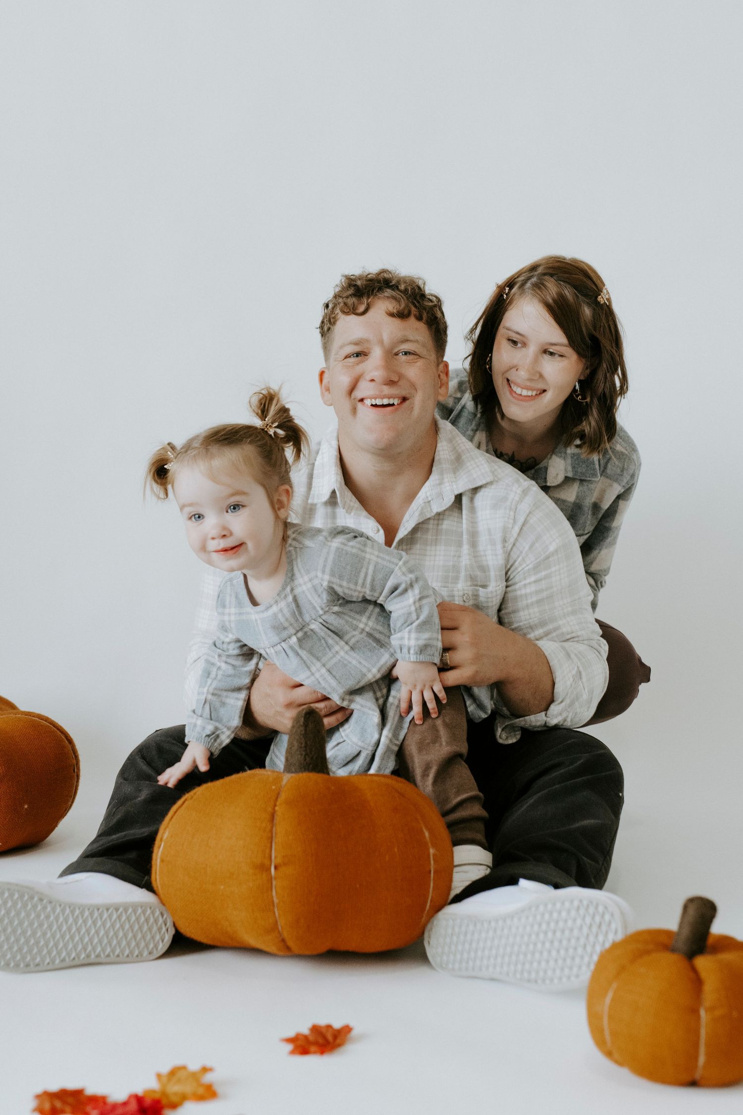 Family poses together with pumpkins and autumn decor on a white background for seasonal portraits.