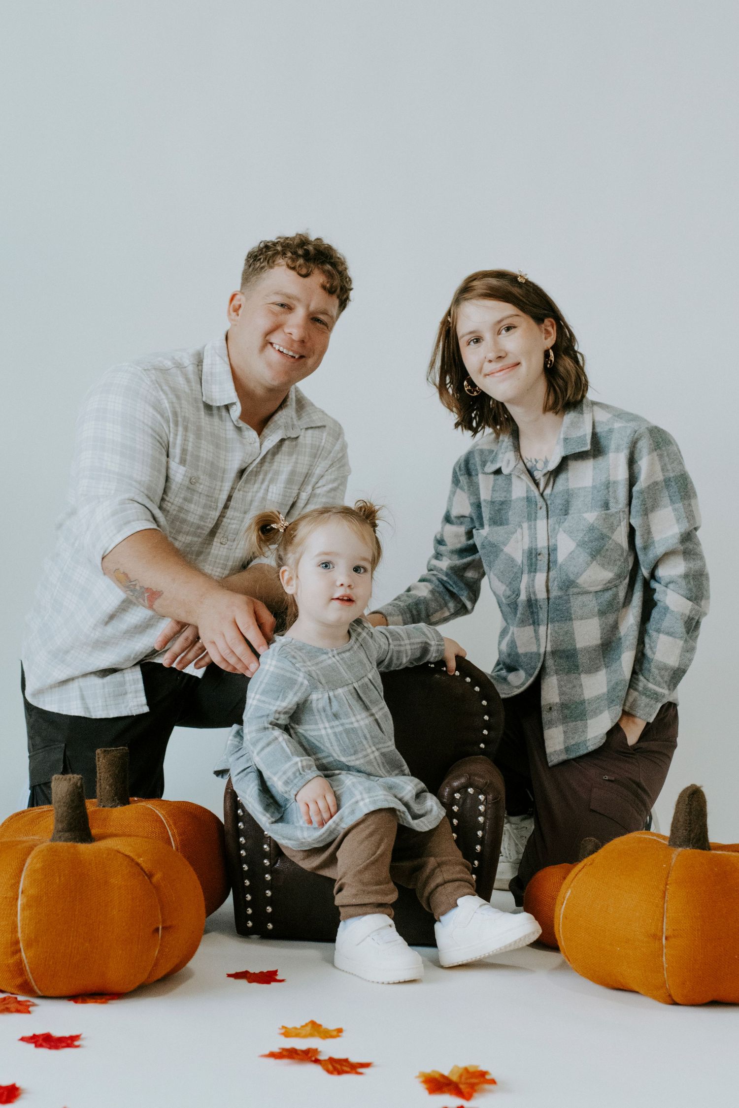 A family photo session with autumn decorations and pumpkins on a white studio background.
