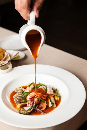 Chef pouring red sauce over seafood dish in elegant white bowl.