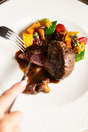 Beef medallions with colorful roasted vegetables on white plate.