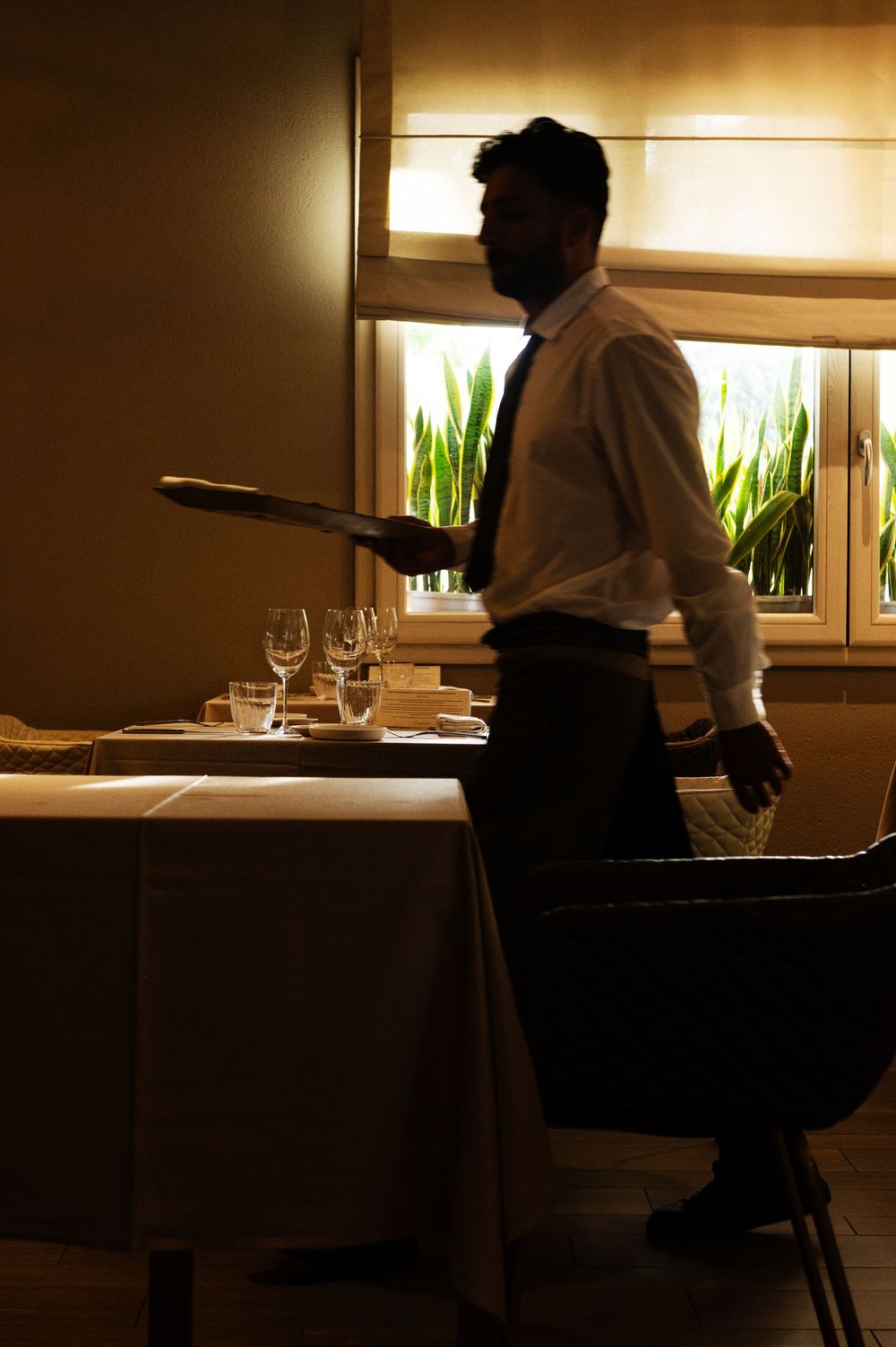 Restaurant interior showing dining tables set with elegant place settings in warm lighting.