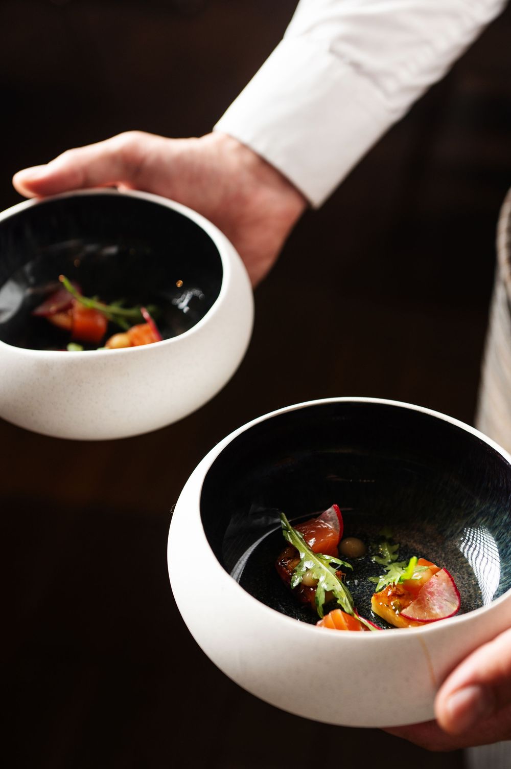 Chef presenting a modern dish in a sleek black and white bowl with colorful ingredients.