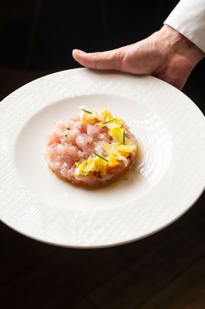 Fresh seafood tartare garnished with yellow edible flowers on a white plate.