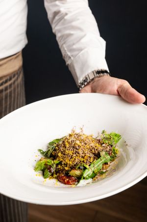 Fresh salad with crispy toppings and microgreens served on white plate.