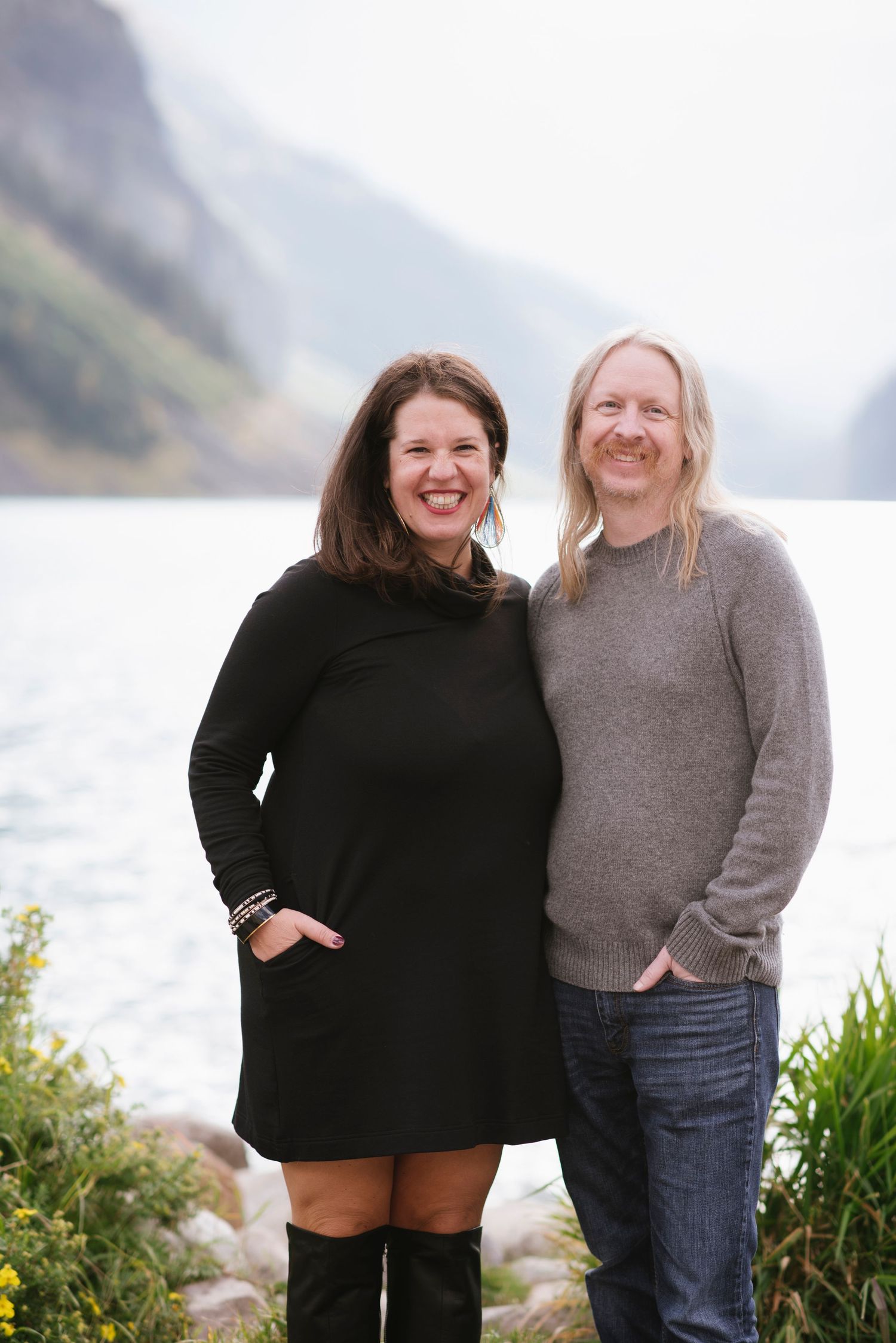 A couple embraces while standing on the rocky shores of Lake Louise in Banff National Park with mountains in the background.