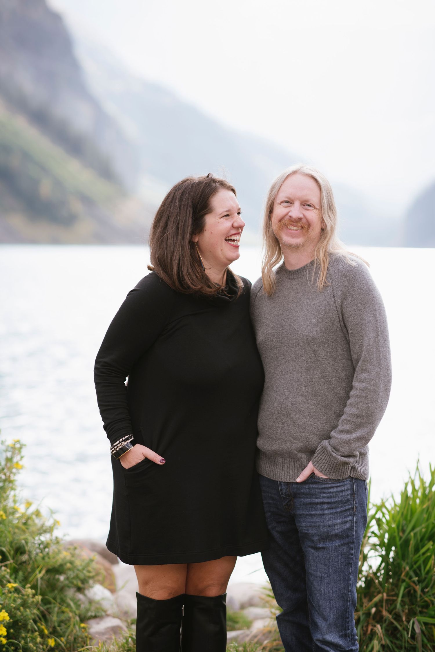 A couple embraces while standing on the rocky shores of Lake Louise in Banff National Park with mountains in the background.