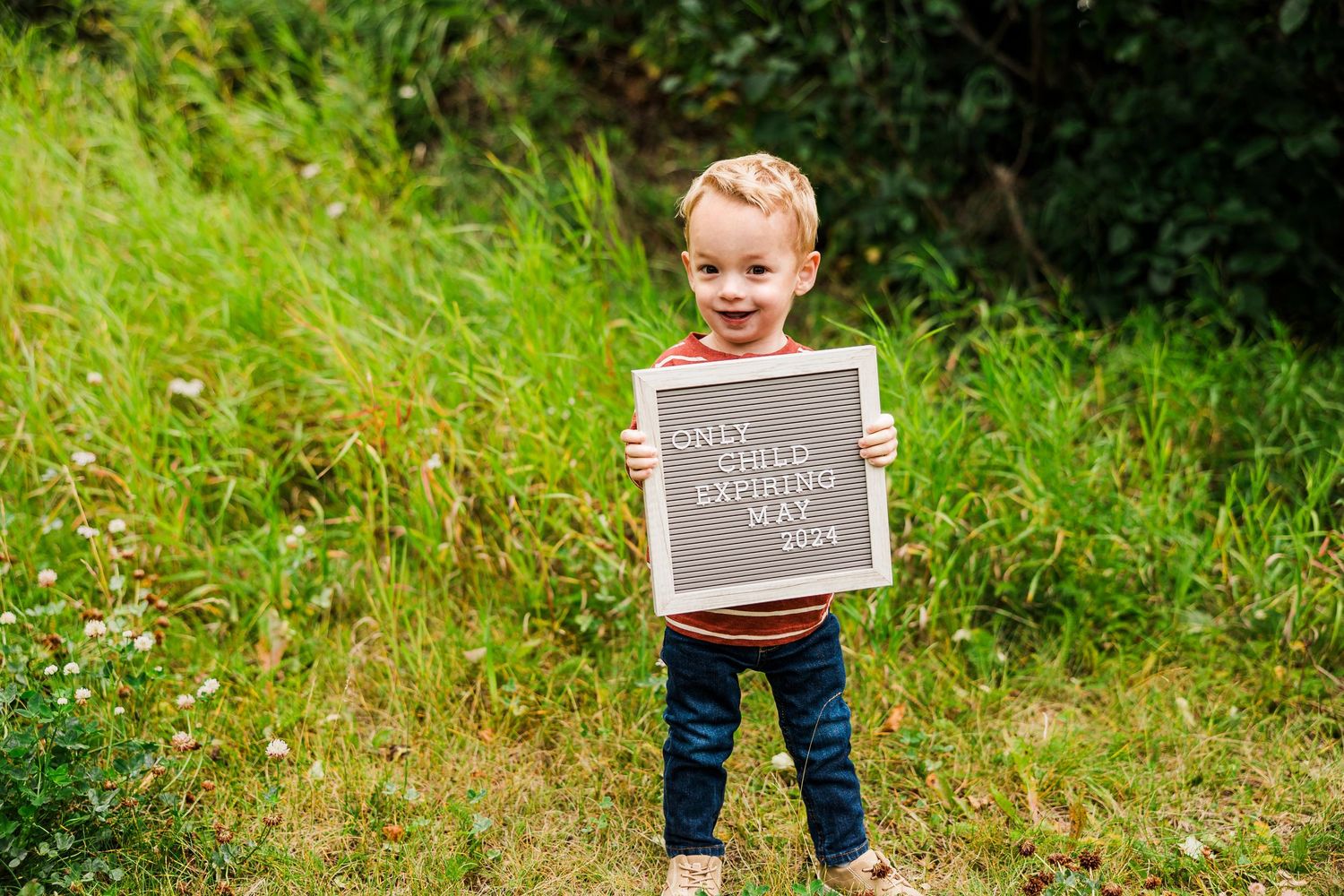 Small child holding a chalkboard sign outdoors in a lush green garden setting.