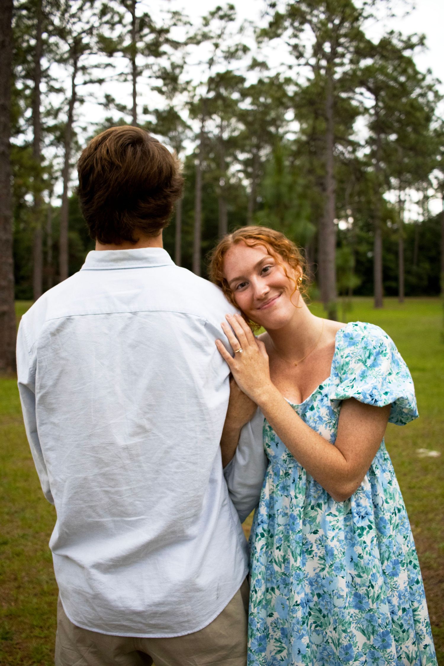 Couple sharing a tender moment outdoors with one wearing a blue floral dress and another in white.