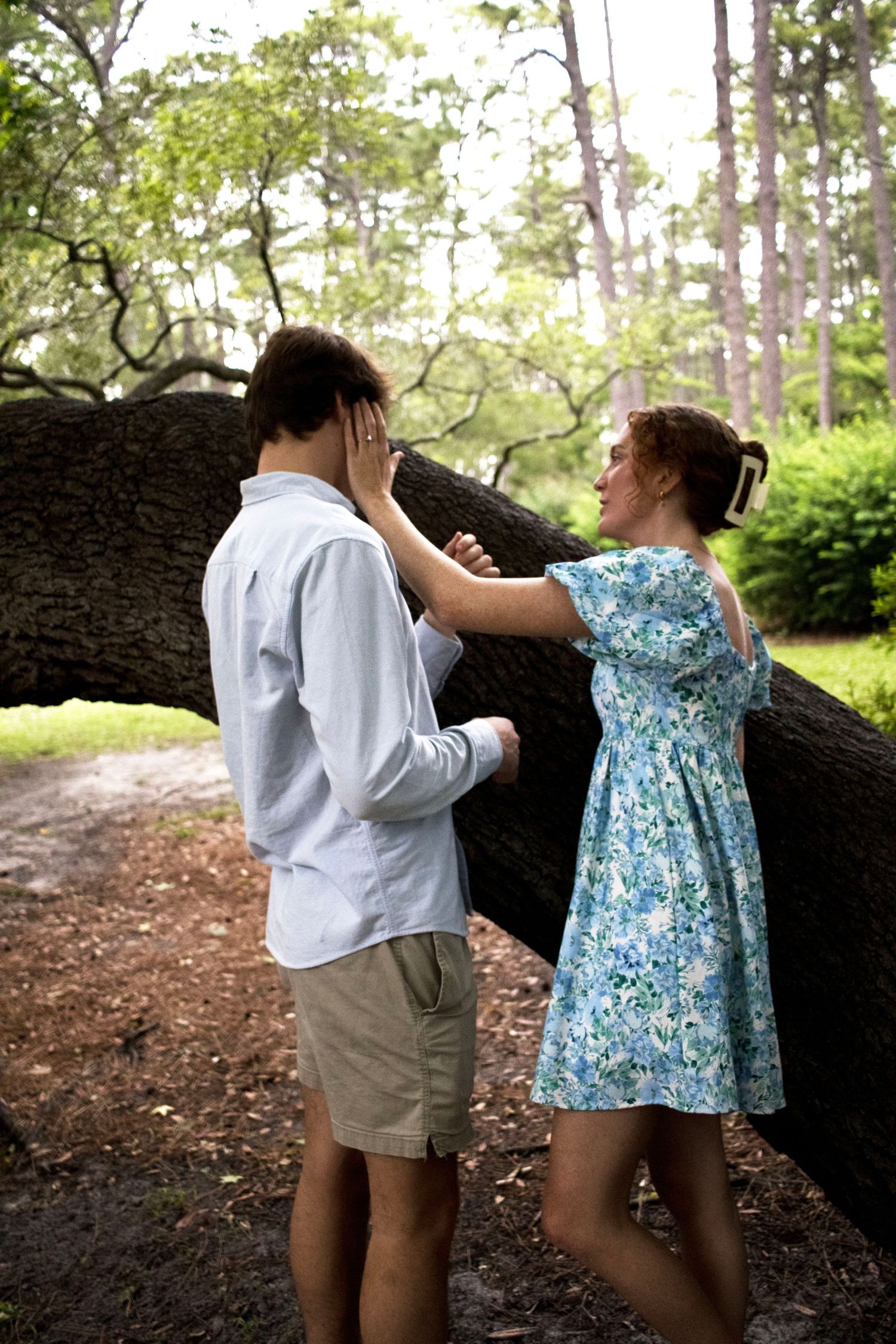 Playful interaction between two people wearing summer clothes near trees.