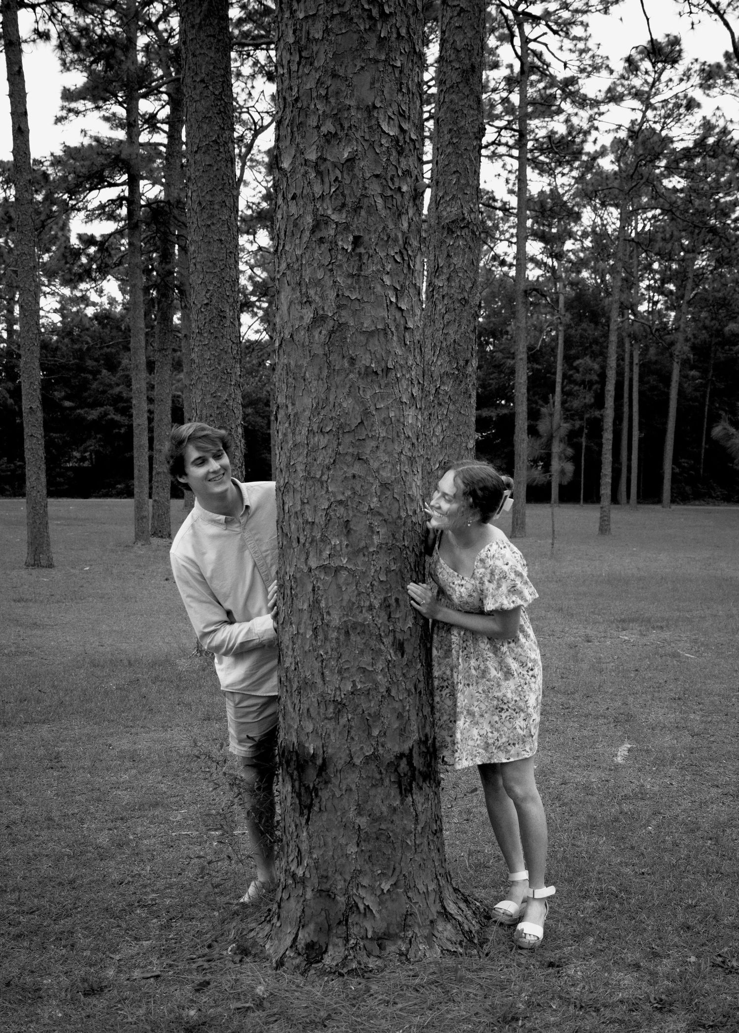Black and white photo of two people playing around large tree trunks in a park.