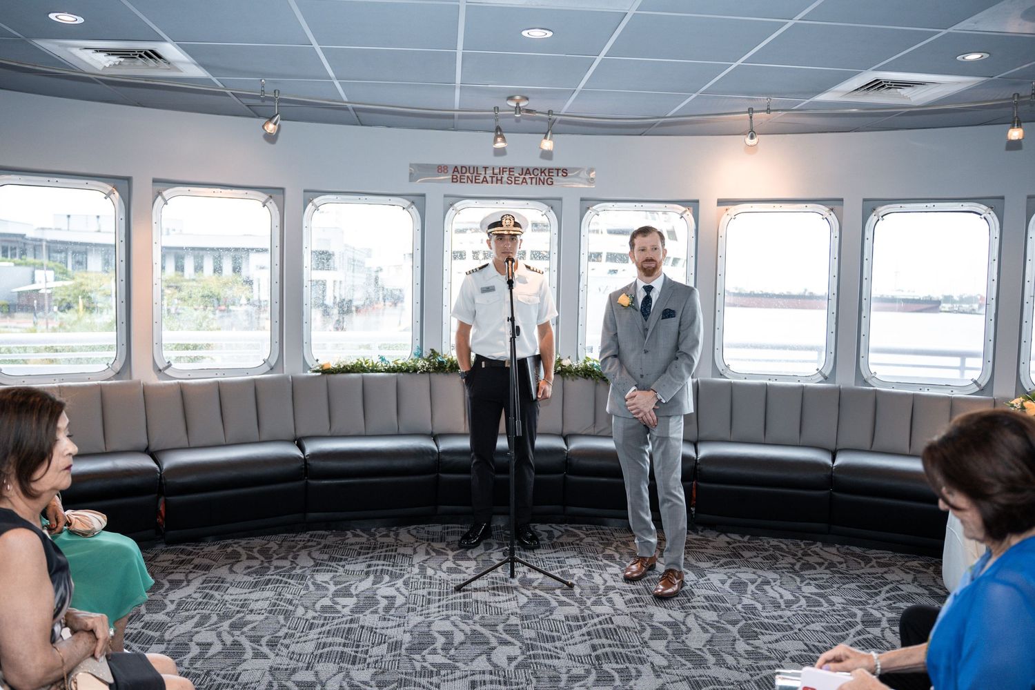 Wedding ceremony taking place in an elegant boat cabin with curved bench seating and nautical windows. Micro wedding on Yacht StarShip in Ta