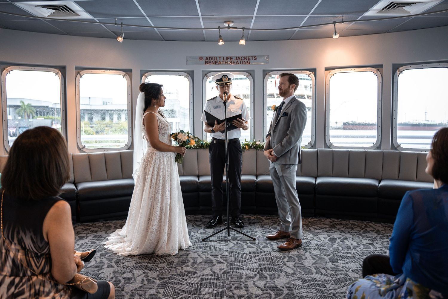 Wedding party celebrating and embracing during a reception on a boat with large windows and water views. Micro wedding on Yacht StarShip in