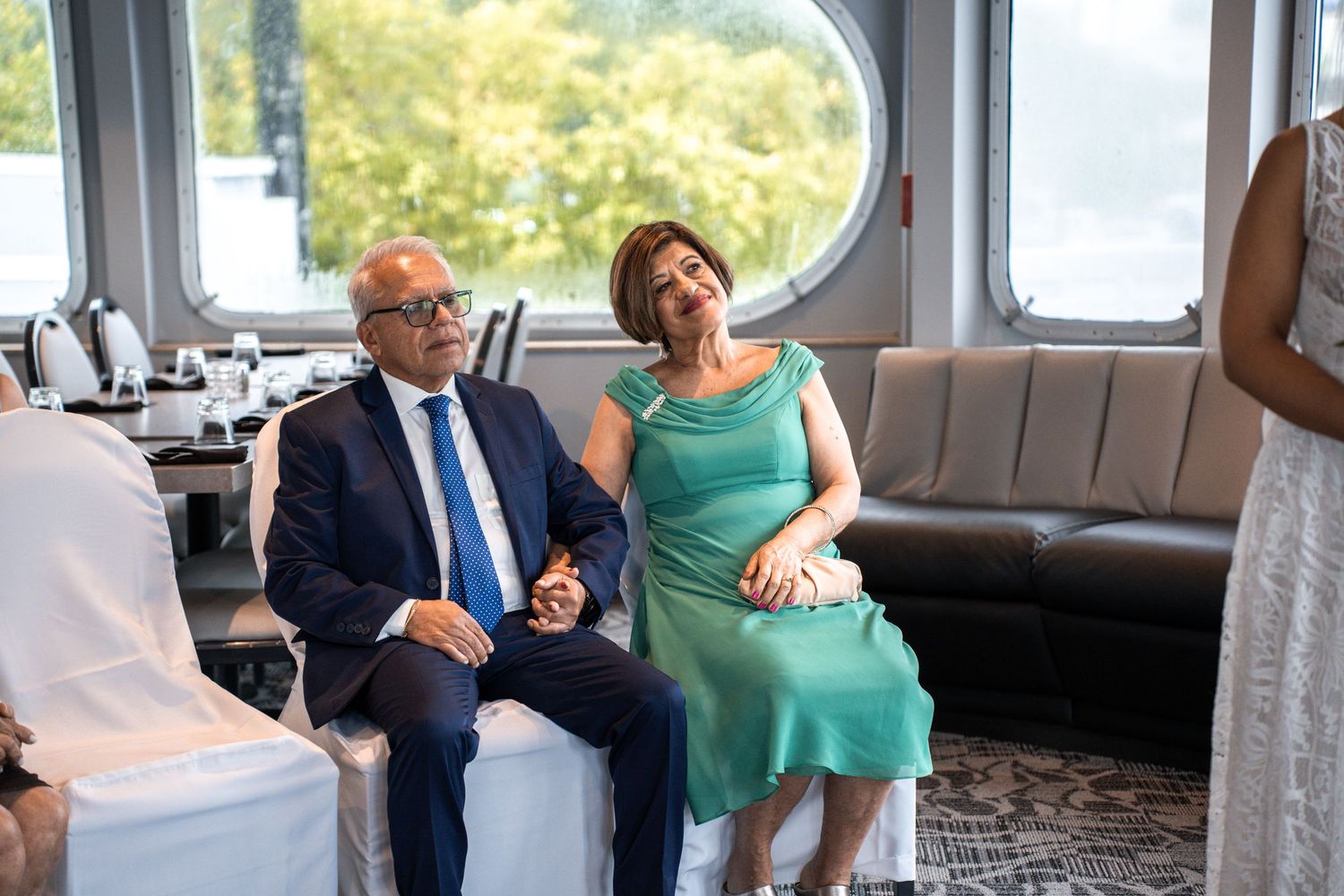 Wedding guests seated on curved bench seating inside nautical venue with round windows. Micro wedding on Yacht StarShip in Tampa