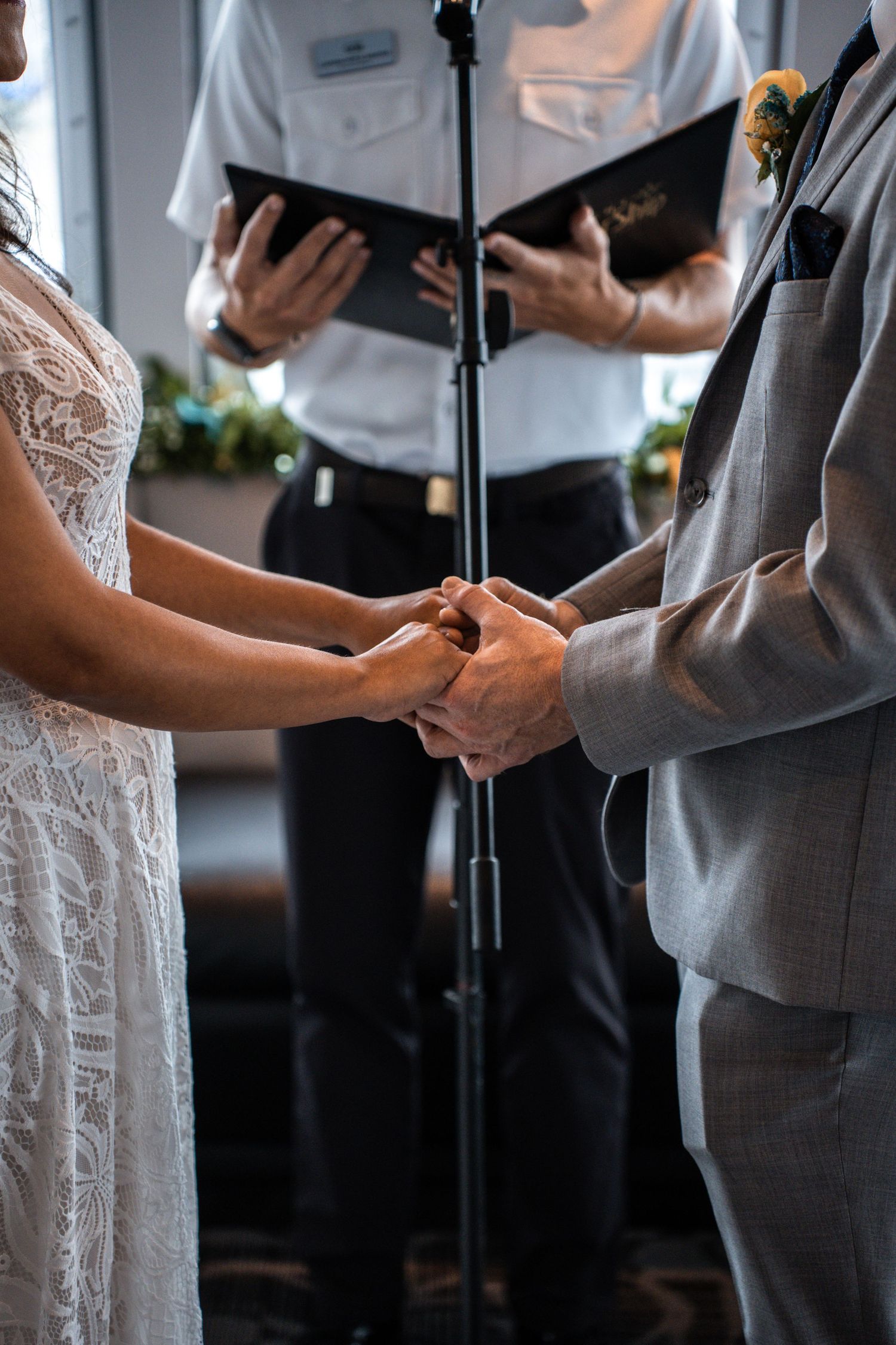Close-up of couple holding hands during wedding ceremony with white lace dress and gray suit details. Micro wedding on Yacht StarShip in Tam