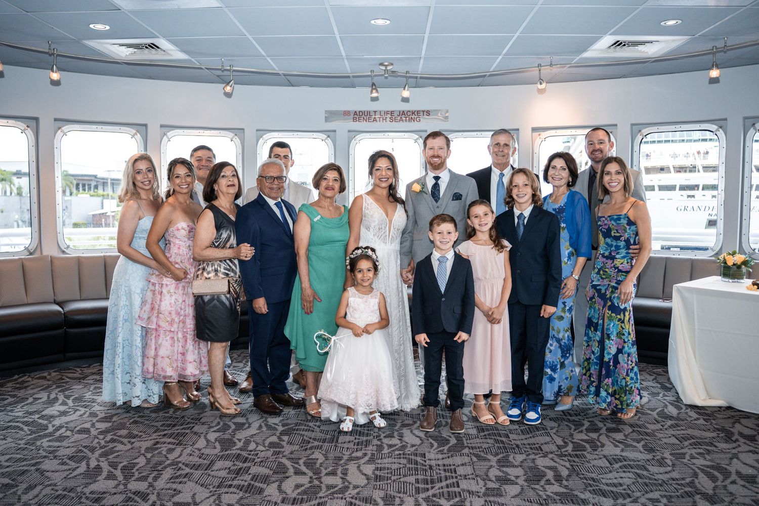 Group photo of wedding party and family members gathered inside boat venue with waterfront views. Micro wedding on Yacht StarShip in Tampa