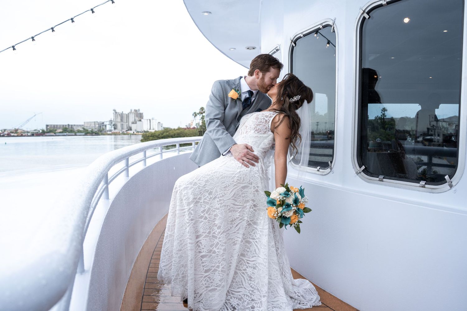Wedding guests gathered on a boat deck with string lights and large windows overlooking the water. Micro wedding on Yacht StarShip in Tampa