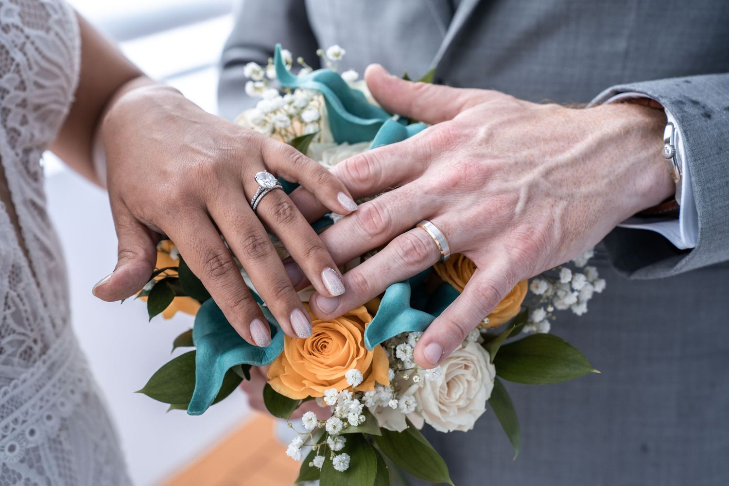 Wedding ceremony detail showing hands exchanging rings with orange and white floral bouquet. Micro wedding on Yacht StarShip in Tampa