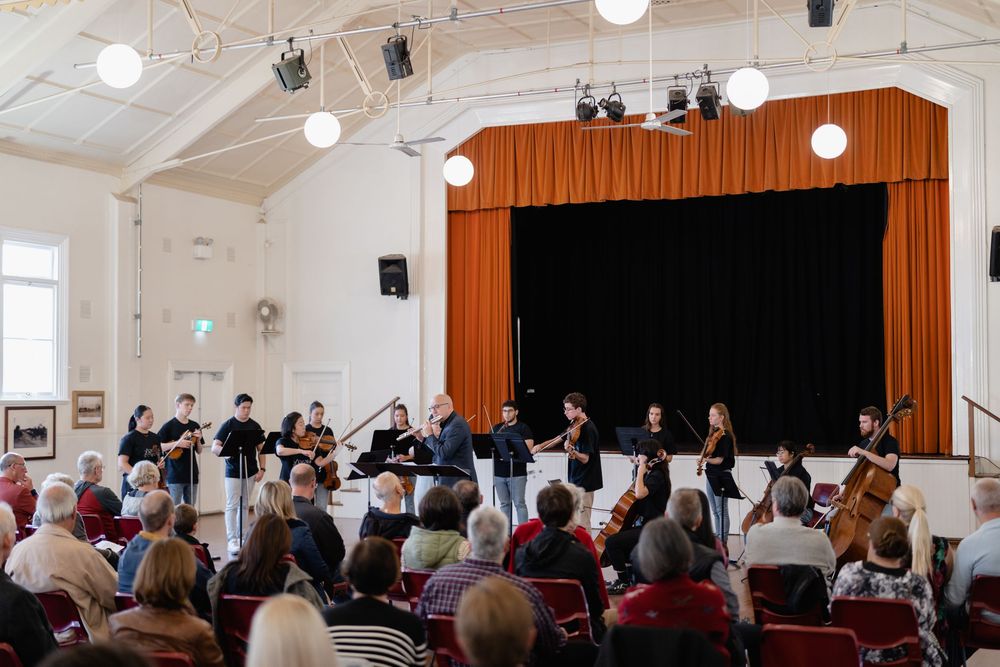 Interior view of a community hall with people seated for a performance.
