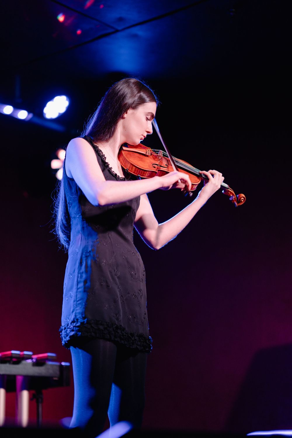A violinist performs on stage under dramatic blue lighting during a concert performance.