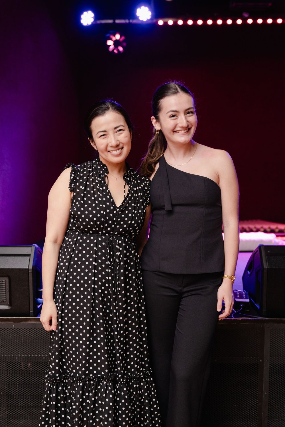 Two performers posing together on stage with theatrical lighting in the background.