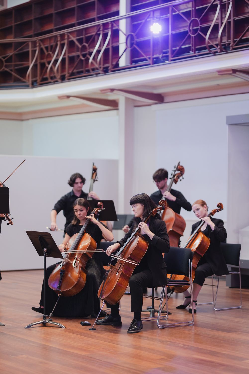 Cellists performing in a line on a wooden floor during a classical music concert.