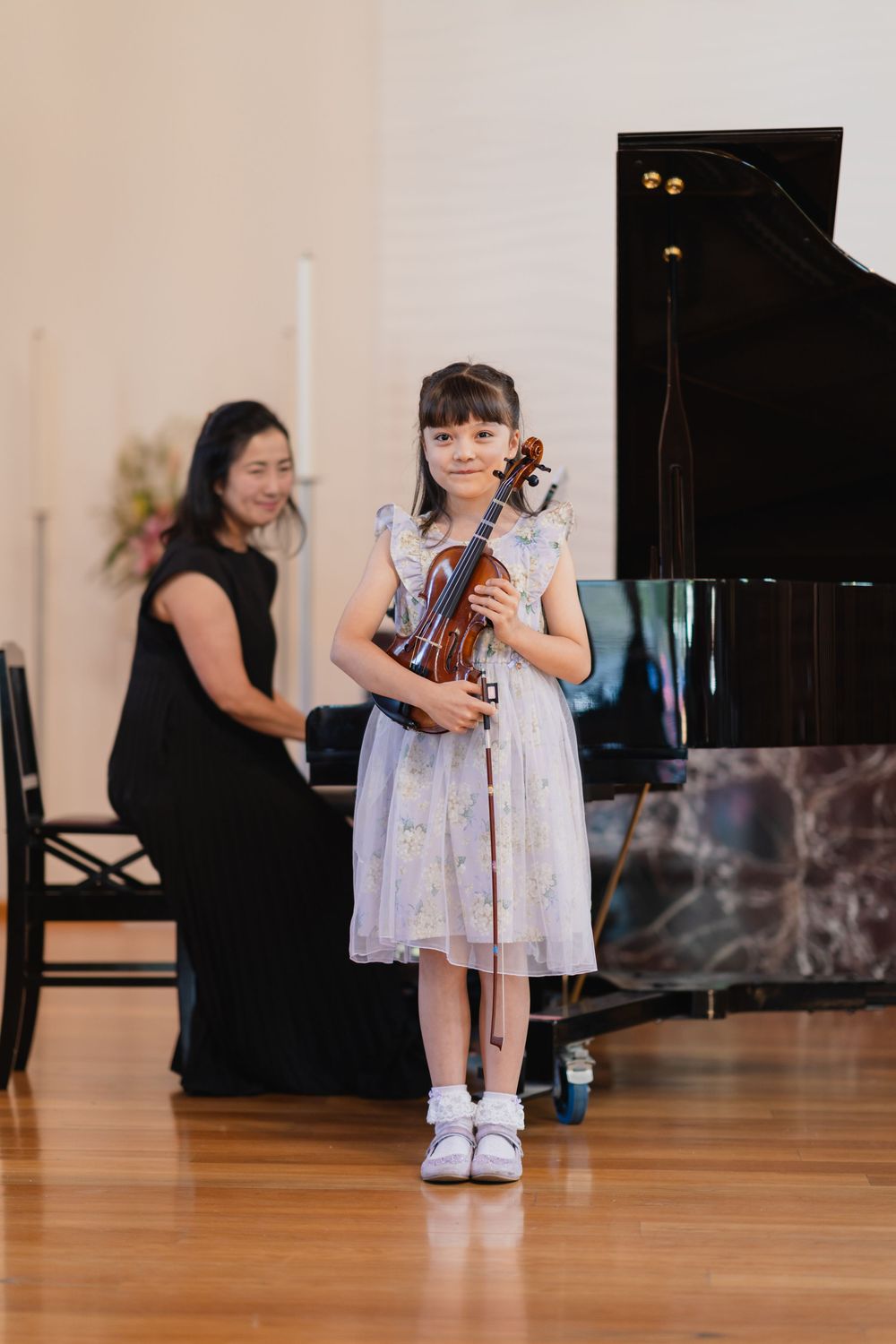 A young performer in a light dress stands in a bright performance space.