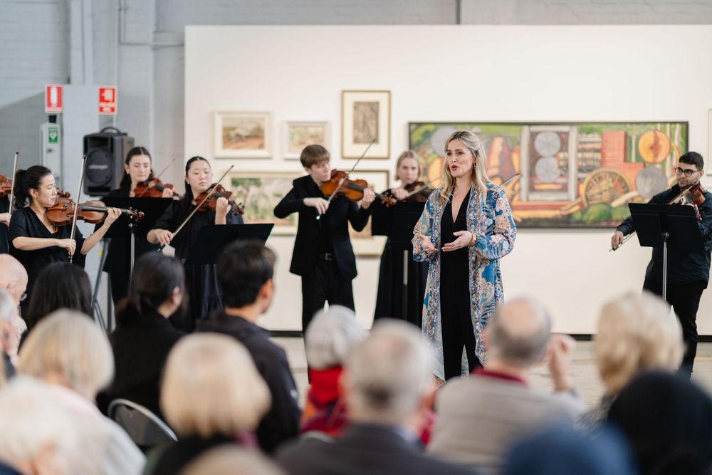 Classical musicians perform in an art gallery with framed artwork visible on the walls behind them.