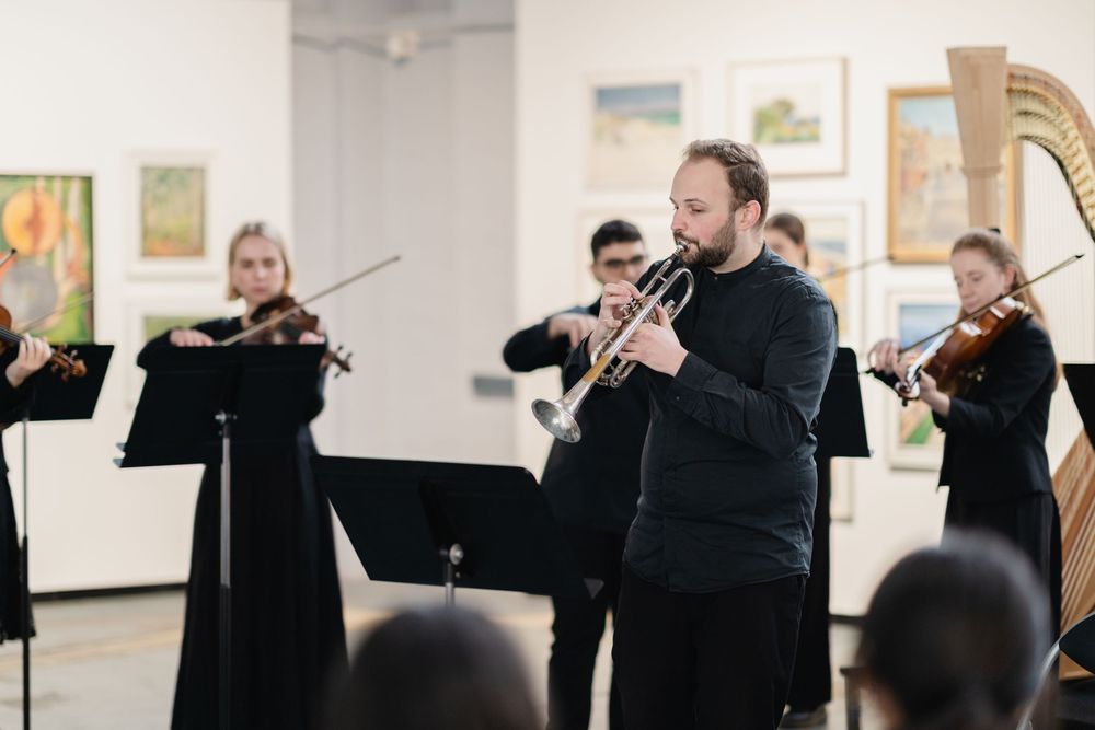 String ensemble performs in a bright gallery space surrounded by artwork on display.
