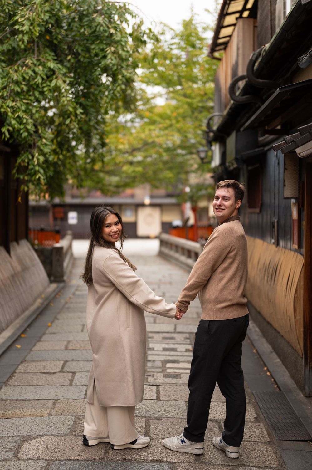 Couple holding hands and looking back while standing in a scenic Japanese alleyway in Kyoto.