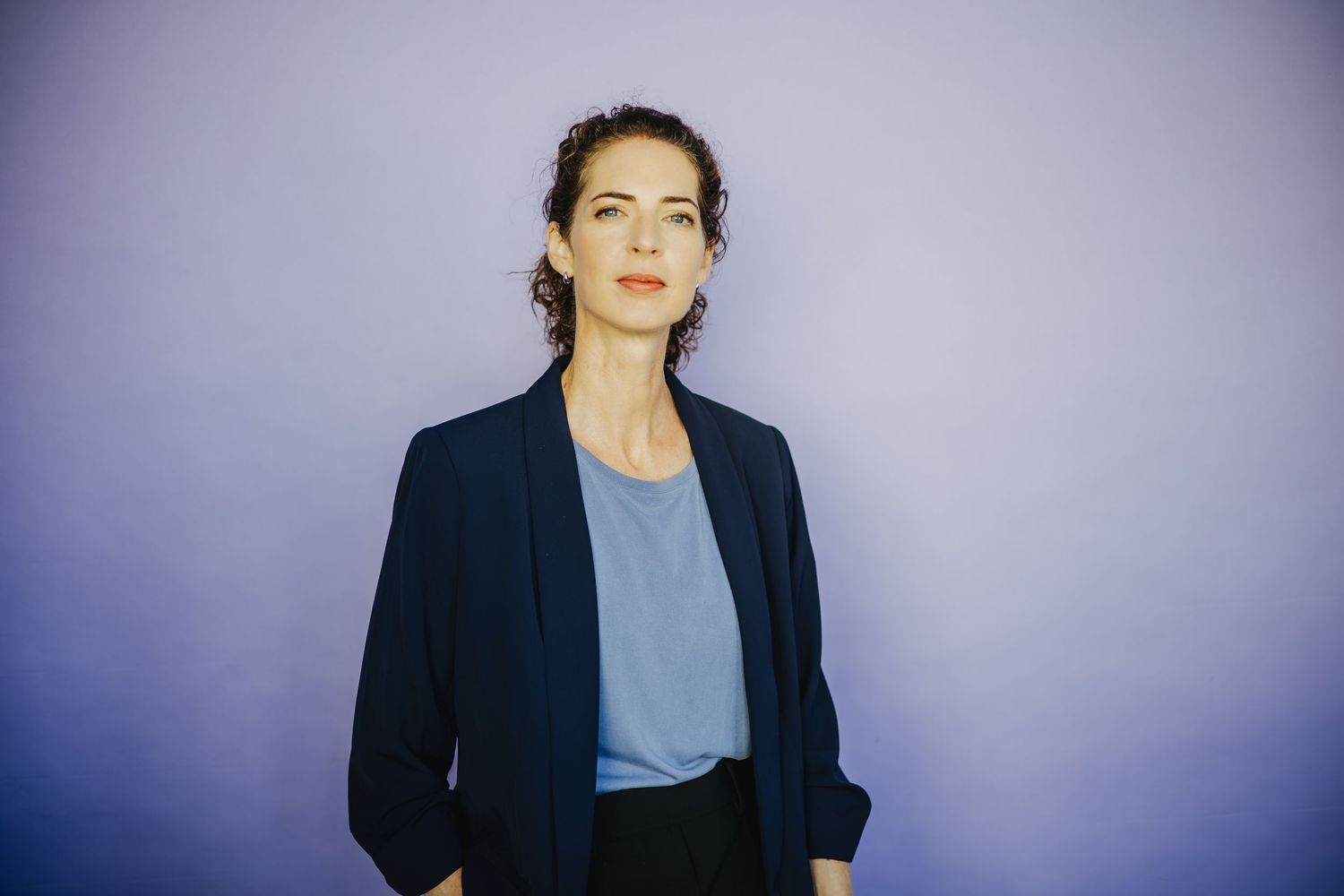 Professional studio portrait in navy blazer against purple background.