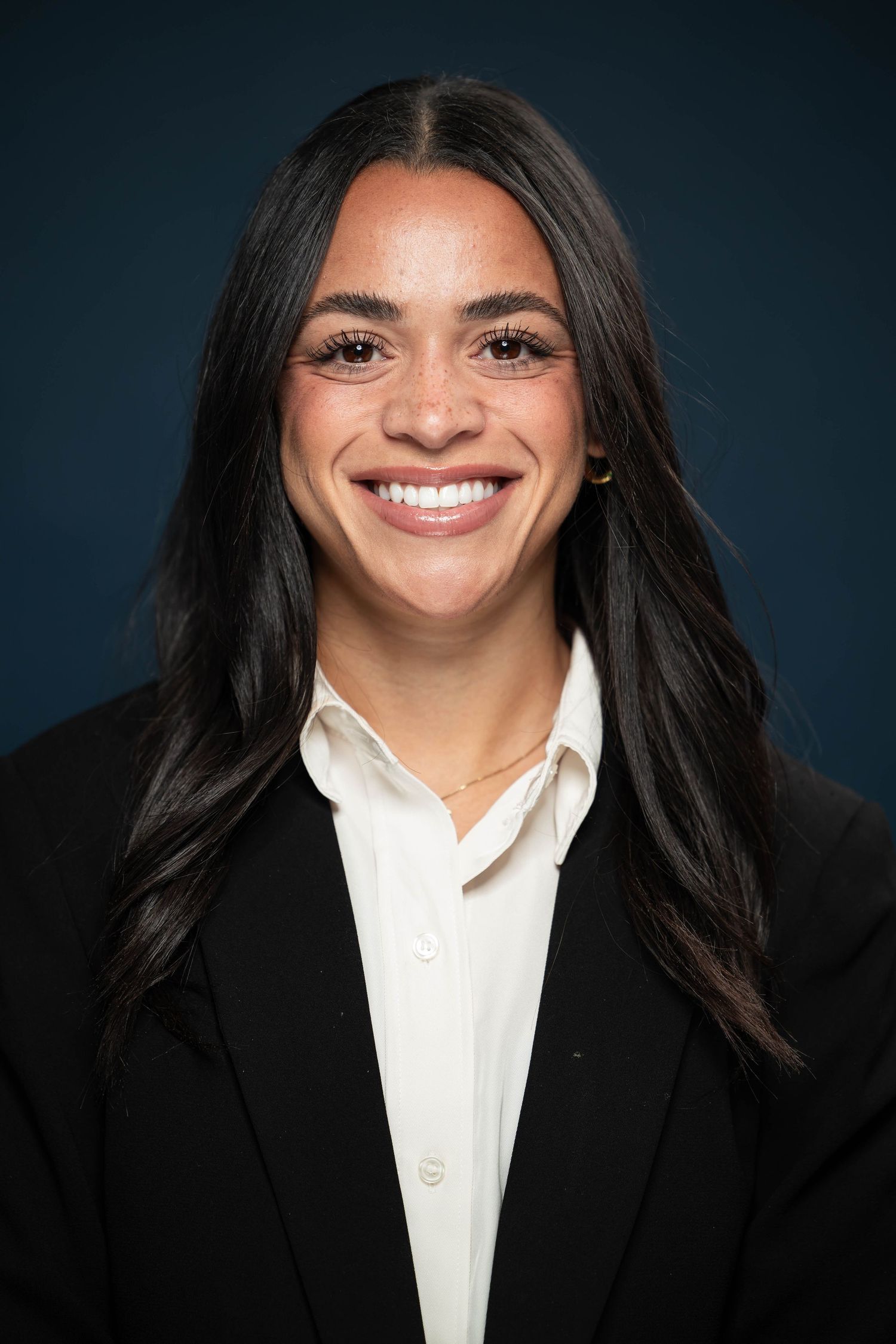 Professional headshot series showing bright smile and dark hair against navy backdrop wearing white collared shirt and black blazer.