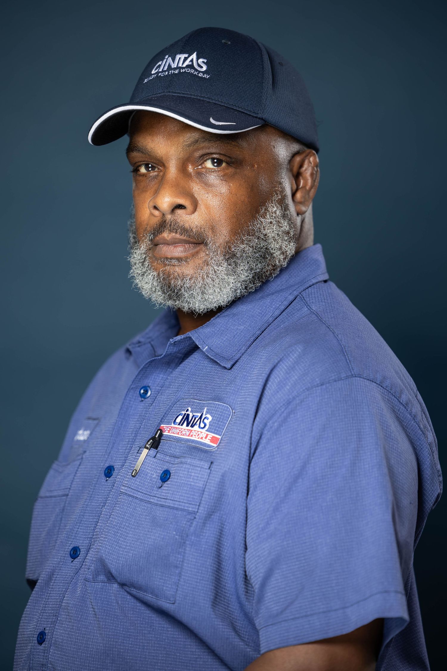 Portrait series showing person in blue work uniform and baseball cap with gray beard against dark background.