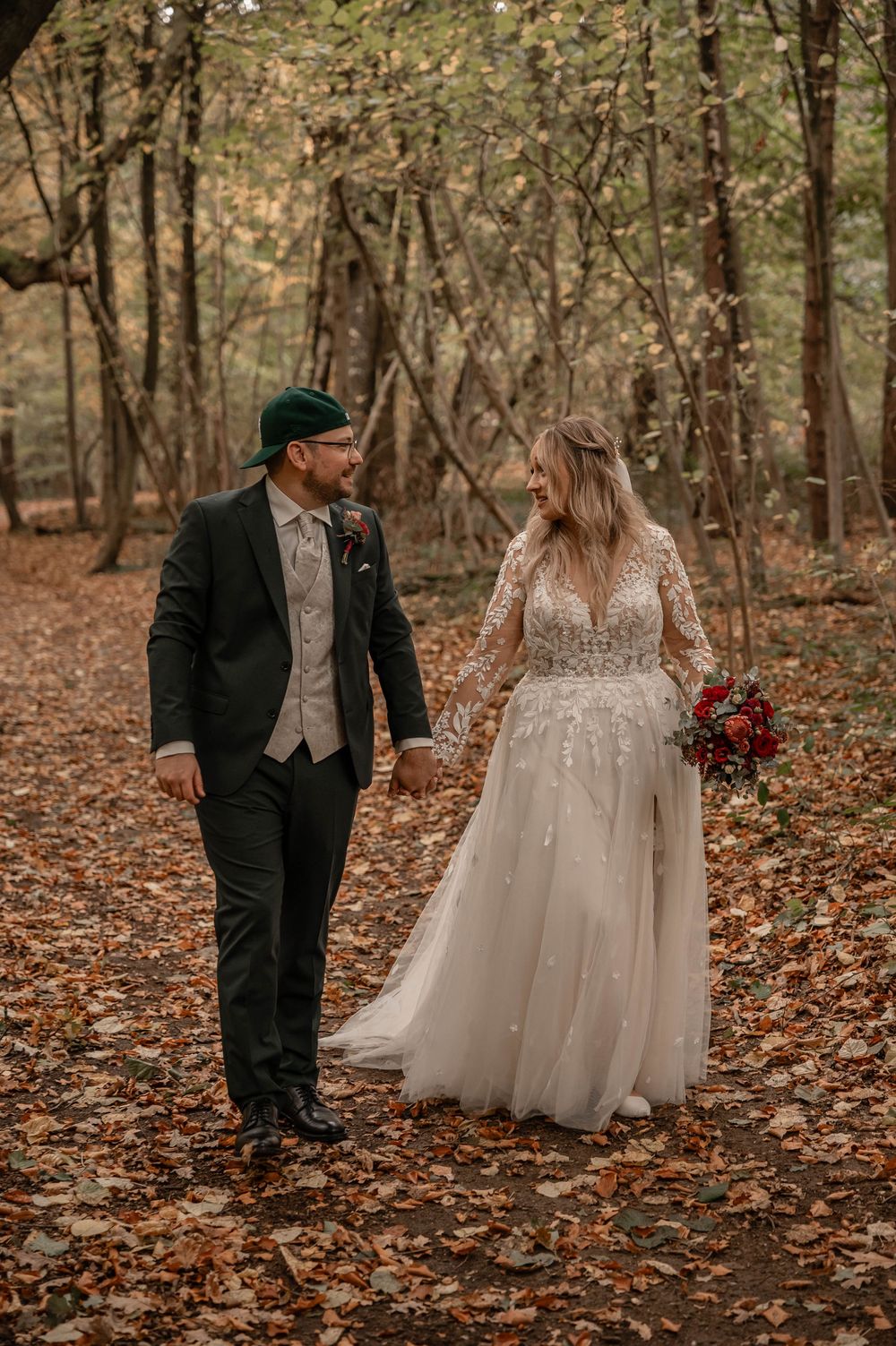 A couple shares a romantic moment among fallen autumn leaves in a wooded setting.