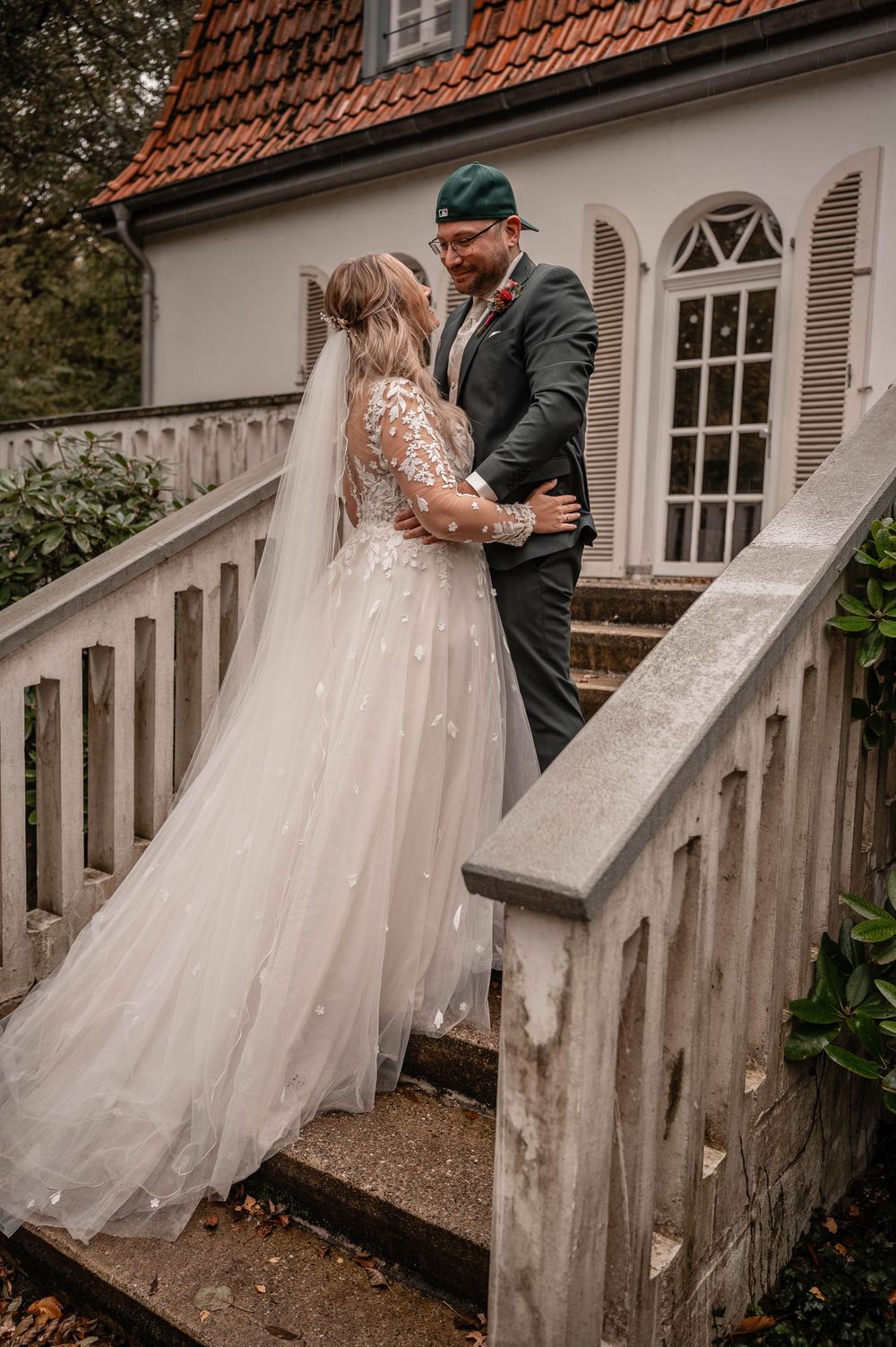 Romantic wedding portrait on white house steps with couple in elegant attire against rustic architecture.