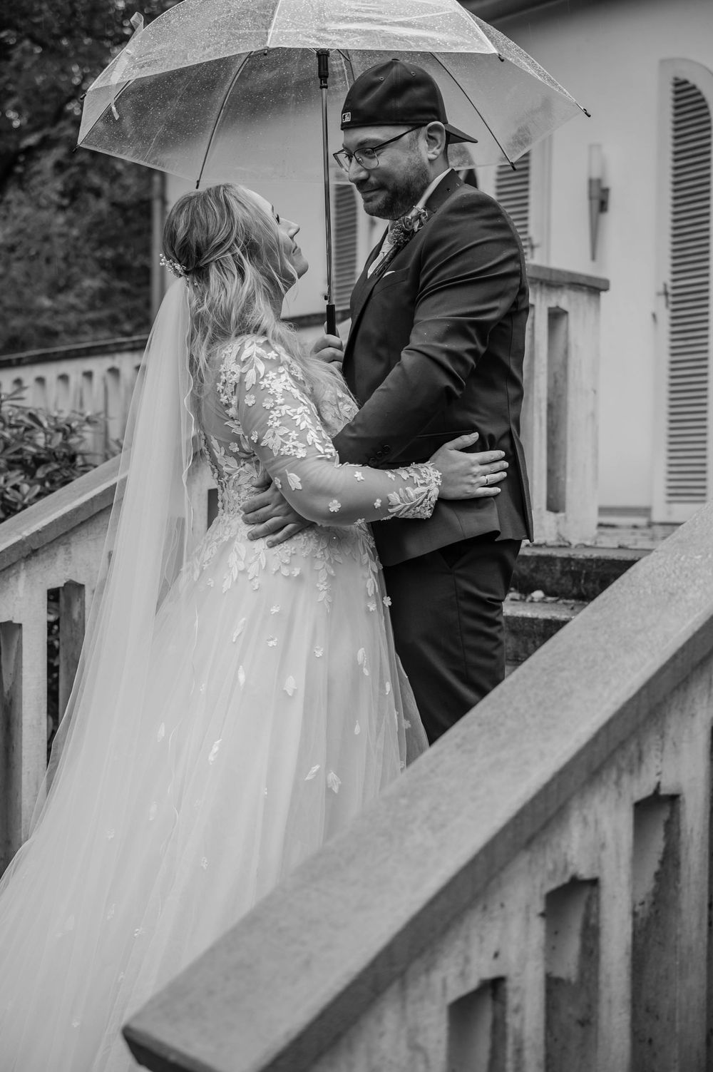 Black and white wedding portraits captured on stairs with an elegant bridal gown and umbrella.