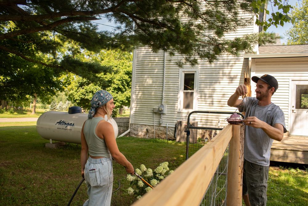 A couple smiling at each other while doing yard work across a fence in Charlotte, Michigan