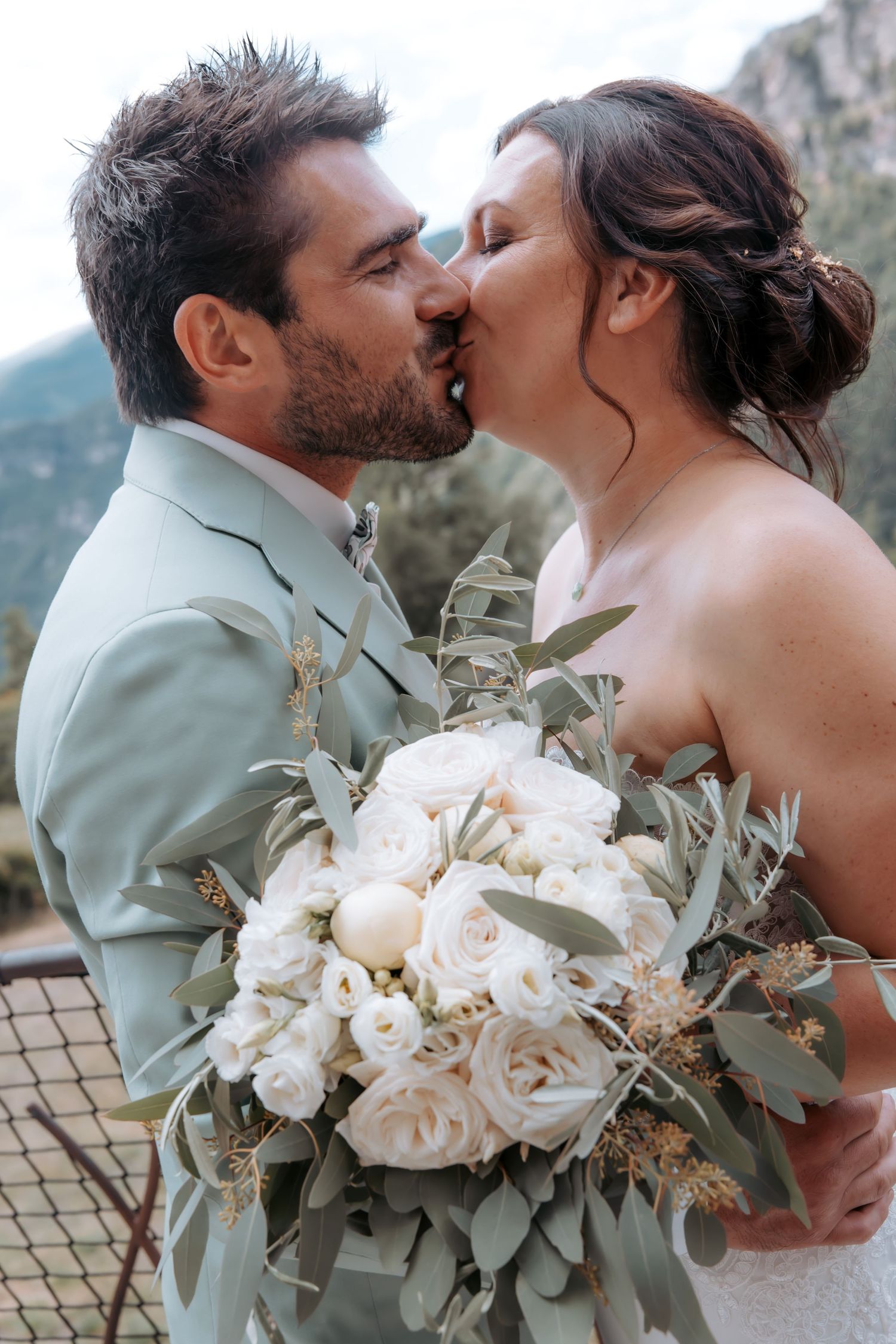 Romantic wedding couple sharing tender moments with white rose bouquet against natural backdrop.