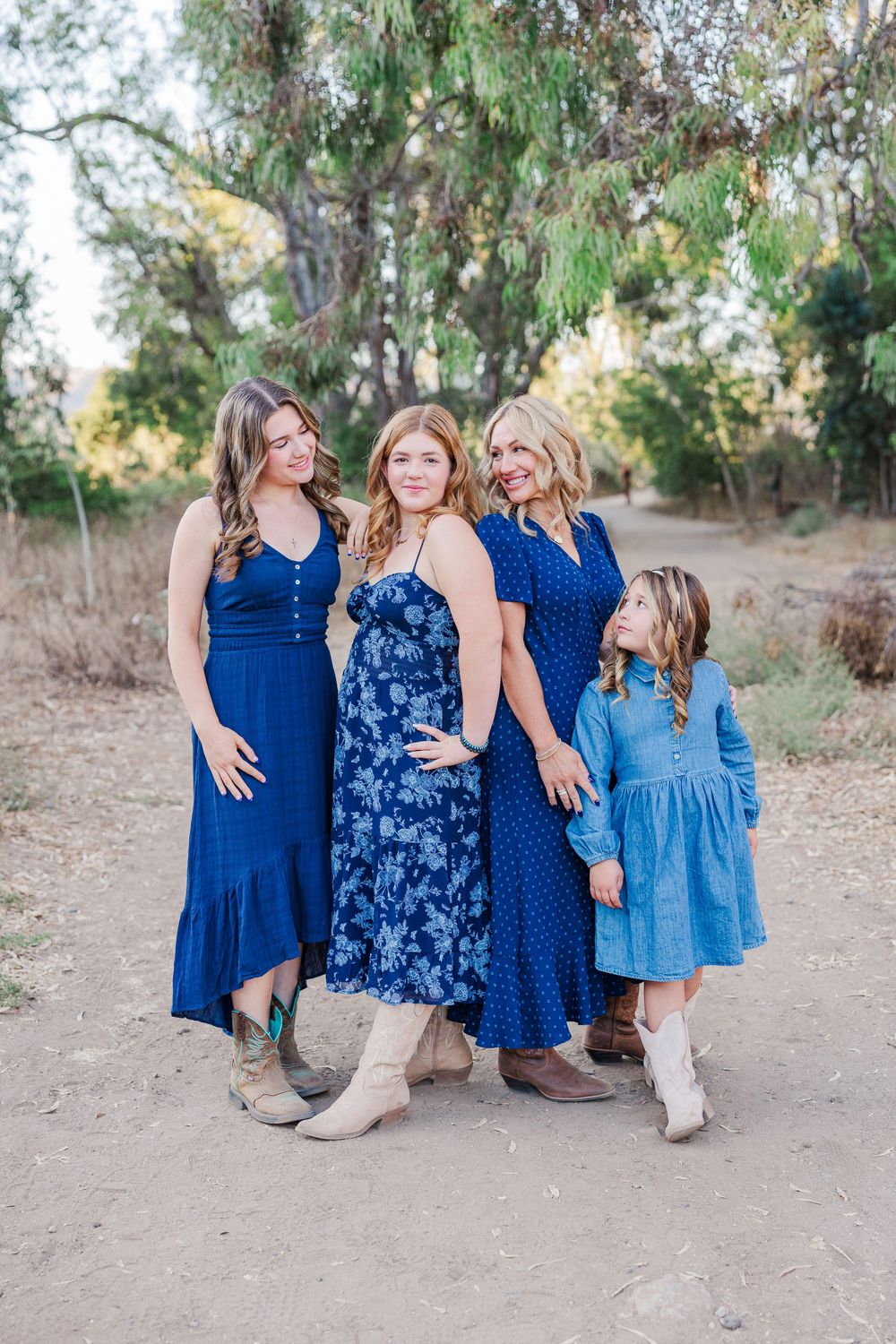 Group portrait of family members in blue dresses sitting together on a dirt path surrounded by greenery.