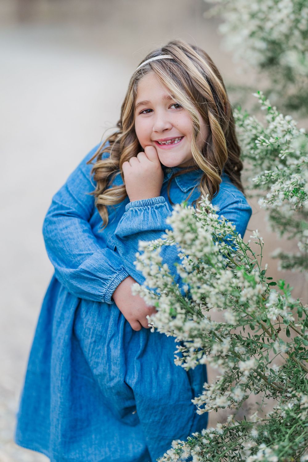 Multiple shots of someone wearing a blue denim dress posing playfully near blooming white flowers in an outdoor setting.